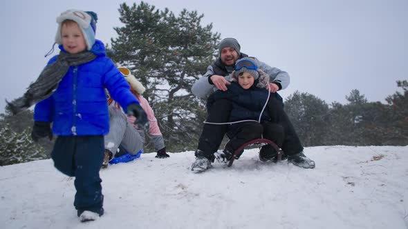 Winter Holidays Joyful Family Having Fun with Children Sledding Down the Slope in the Snowy Forest