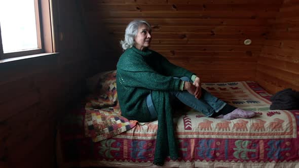 Elderly Woman Sits in a Wooden Room and Alone Looks in Different Directions