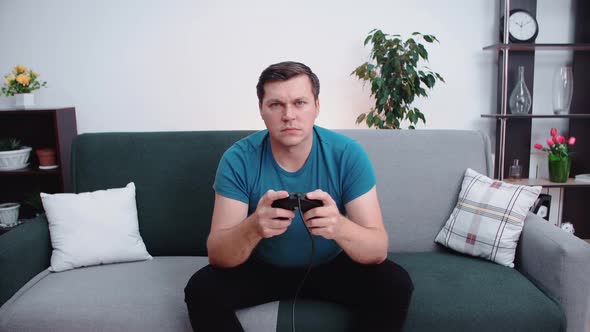 A man is sitting on the couch in front of the TV, holding a joystick in his hands