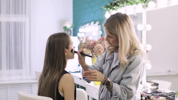 Makeup Artist Is Applying Base Tone Cream on Woman's Face Using Brush