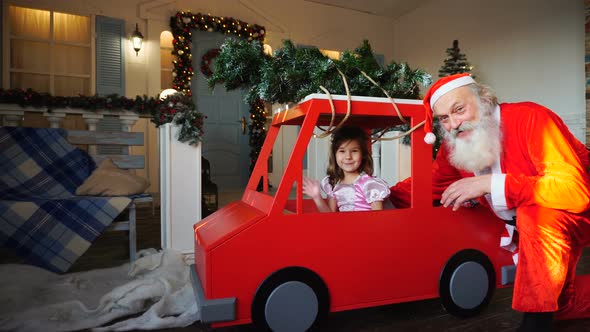 Funny Santa Claus Playing with Little Princes Waving Hand in Red Car.