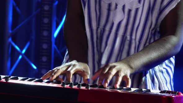 African American Man Plays Piano Synthesizer and Sings in Dark Studio with Blue Lights alt