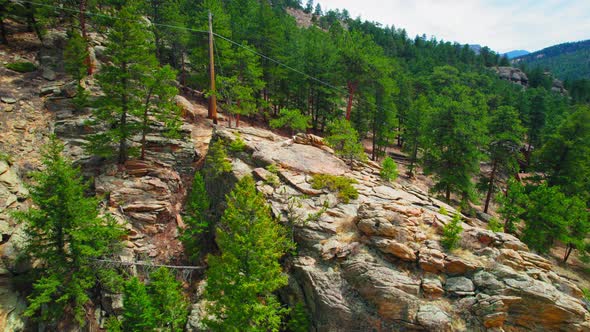 Aerial Shot Of Mountain Goat Laying On Top Of Rocky Mountain Hillside Cliff Surrounded By Lush Green alt