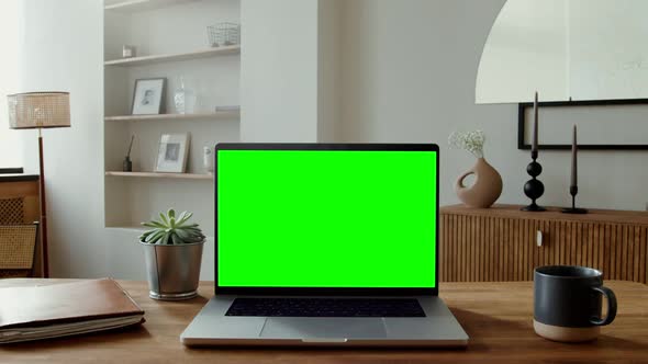 An Open Laptop with a Green Screen Standing on a Table in a Home Interior alt