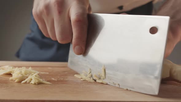 Front View of Young Man Chef Cut Thin Slices of a Piece of Ginger with Knife alt