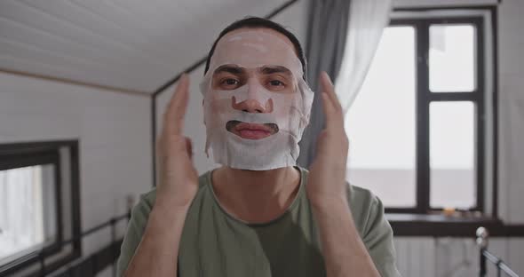 Portrait of a Young Man Using a Fabric Moisturizing Face Mask at Home alt