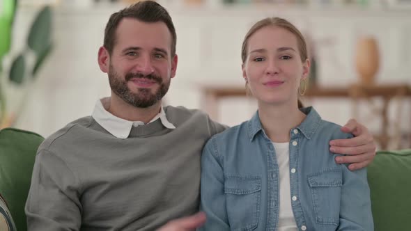 Positive Couple Showing Thumbs Up While Sitting on Sofa alt