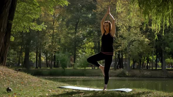 Wide View of Woman Stand on Yoga Mat and Practicing Yoga Stretching Exercise Outdoors in Sunny Day alt