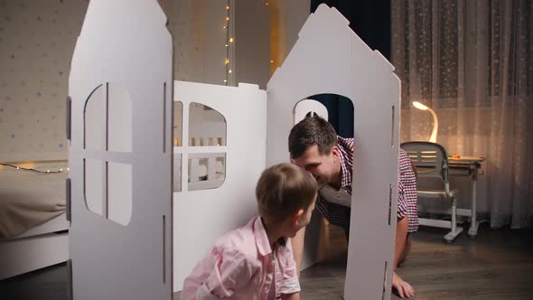 Happy Cheerful and Laughing Boy with Young Father Playing in Toy House in Children Room at Night alt