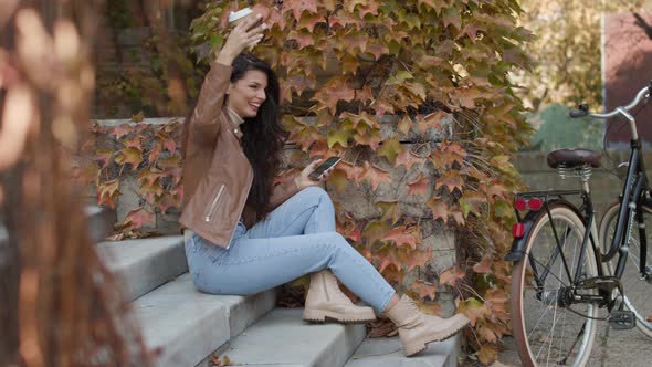 Pretty young woman with mobile phone drink coffee to go by the bicycle on autumn day