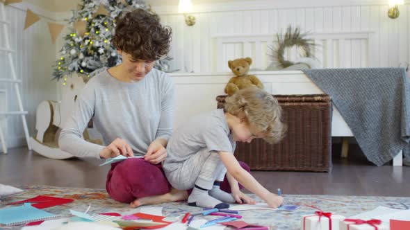 Beautiful Mom and Cute Kid Making Christmas Paper Crafts at Home alt