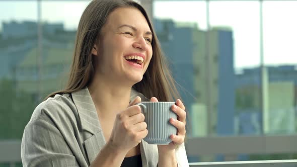 Beautiful Young Businesswoman Drinking Hot Tea or Coffee While Standing on the Office Balcony