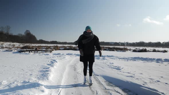 Young woman in black skirt and white figure skates is ice skating on frozen lake alt