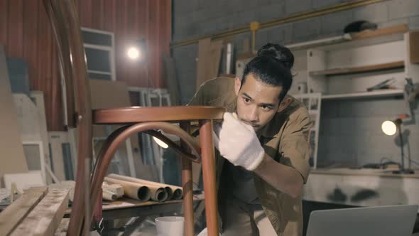 Young Asian man Carpenter uses a tape measure to measure chair on the workbench alt