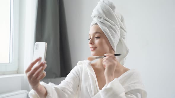 Cute Caucasian Woman Using Makeup Brush and Smiling in Front of Small Mirror