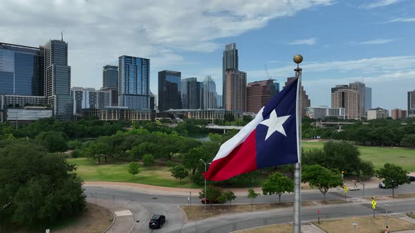 Rising aerial shot of Texas flag in front of Austin, Texas skyline. Walkable green space and park in alt