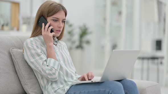 Young Woman with Laptop Talking on Smartphone at Home alt