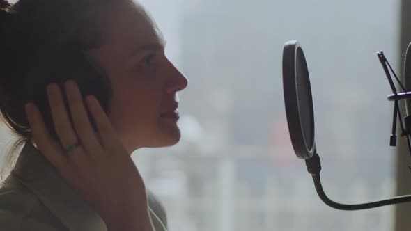 A Young Girl Emotionally Sings Into a Microphone in the Background of the Window alt