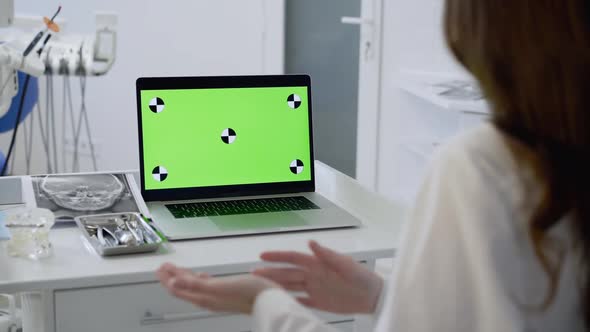 Female Dentist Conducts Online Consultation with Gestures at Laptop at Table alt
