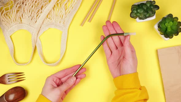 Hands of a young woman holding a metal reusable eco-friendly straw for drinks on a yellow background