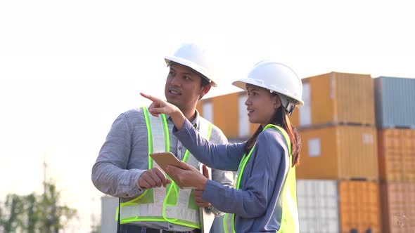 Two logistic staff discussing while checking and control loading containers box from cargo.