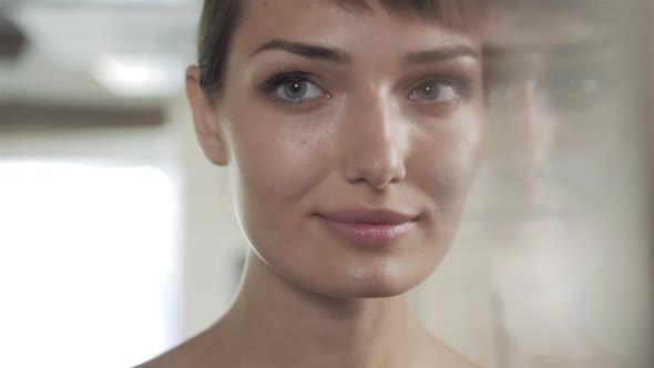 Woman in a Beauty Salon Looks at Her Reflection in the Mirror with Lamps and Checks Hairstyle and alt