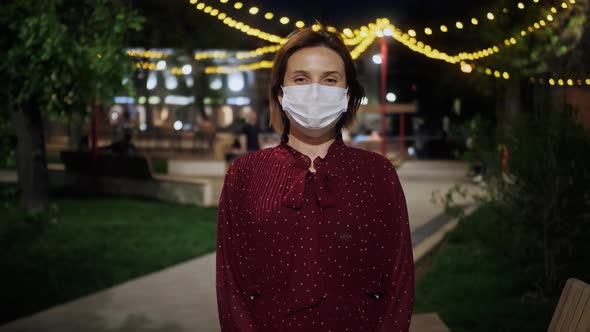 Portrait of a woman out and about in the city streets during the evening, wearing a face mask. alt