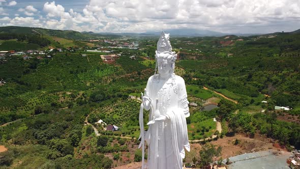 Aerial of White Lady Buddha Statue with Mountains, Countryside Village and Farm alt