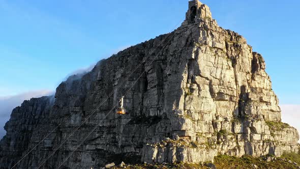 Aerial footage ascending up cliffs following a cable car going up Table Mountain