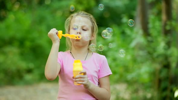 Portrait of funny lovely little girl blowing soap bubbles. Happy carefree childhood. Slow motion