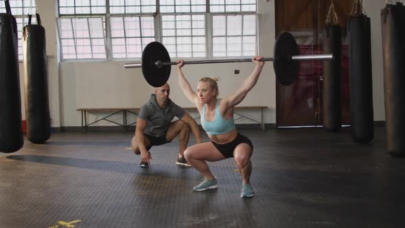 Fit caucasian woman working out with barbell with male trainer at the gym alt