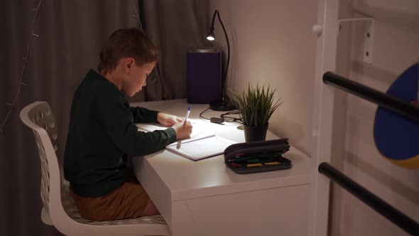 Caucasian Boy Doing Homework at Home By the Light of Lamp alt