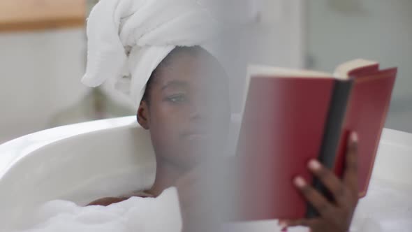 Portrait of african american attractive woman relaxing in bath and reading book in bathroom alt