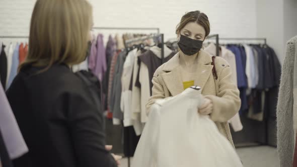 Confident Woman in Coronavirus Face Mask Taking Hanger with Stylish Clothes From Shop Assistant and alt