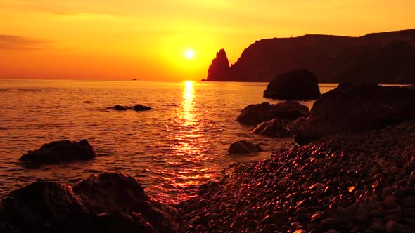 A Red Burning Sunset with the Silhouette of a Cliff Over the Sea alt