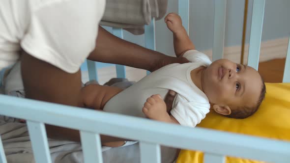 African Young Man Putting Newborn Mixed Race Son in Crib To Sleep alt