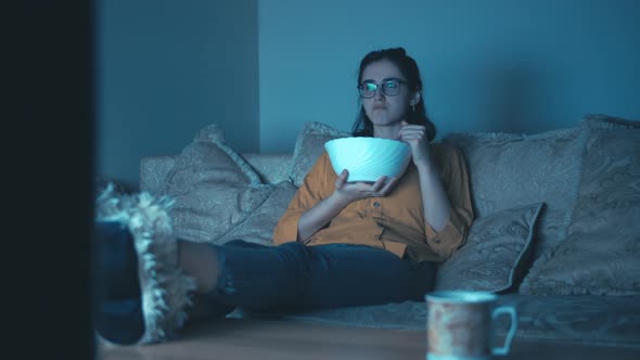 Teen Girl Relaxes in Front of the TV in the Evening Eating Chips and Dancing Moving Camera