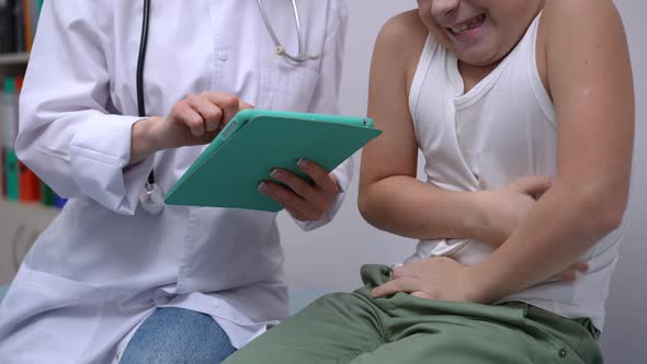 Unrecognizable Boy Complaining Stomach Ache in Hospital As Doctor Filling in Online History alt