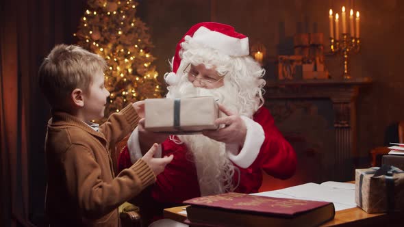 Santa Claus and little boy. Cheerful Santa is working at the table. Christmas concept. alt