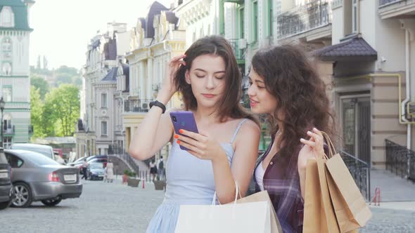 Two Young Female Friends Using Online Map on Smart Phone on City Streets