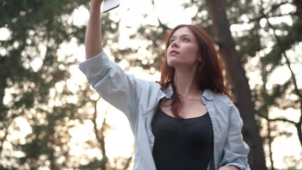 Charming Slim Woman Raising Phone Searching Internet Rejoicing in Sunshine in Forest alt