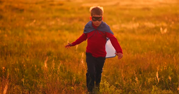 Little Superhero Boy in the Field at Sunset Fantasizes and Dreams. alt