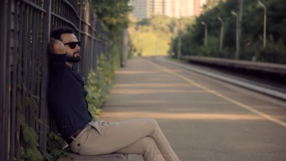 Businessman Relaxing And Sitting On Railway Train Station Platform. Man Passenger Wait Tram. alt