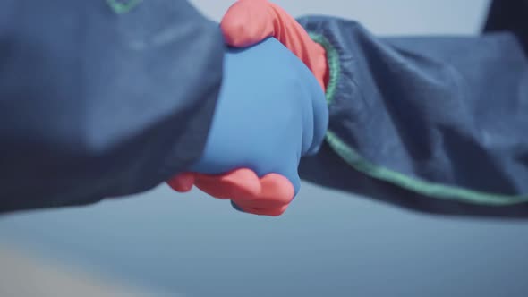Close-up Handshake of People in Chemical Suits and Protective Gloves. Two Unrecognizable Workers alt
