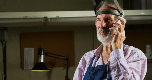 Goldsmith talking on mobile phone in work shop alt