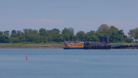 Orange Roll-on, roll-off ferry leaving the prison dock at Hart Island, with white prison bus. Blue s alt