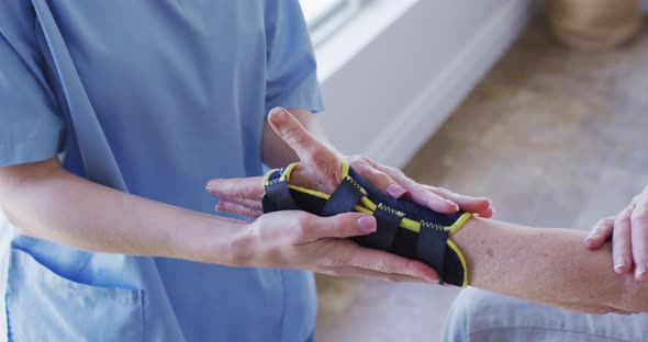 Mid section of female health worker putting face mask on senior woman at home alt