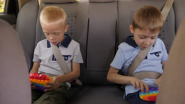 Two Little Brothers are Sitting in the Car and Playing an Antistress Toy Pop It alt