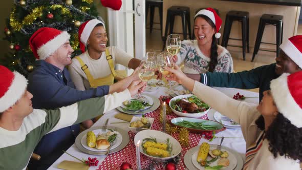 Happy group of diverse friends in santa hats celebrating meal, toasting with vine at christmas time alt