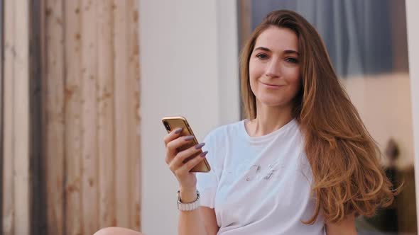 Portrait of Young Woman Using Mobile Phone at House Porch